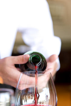 Close up of a waiter\'s hands pouring red wine into a glass