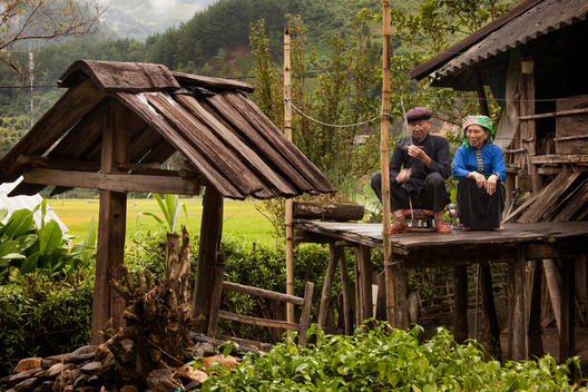 An older man and his wife, members of an ethnic minority tribe, sit on their porch as the man works on his handmade fish nets.
