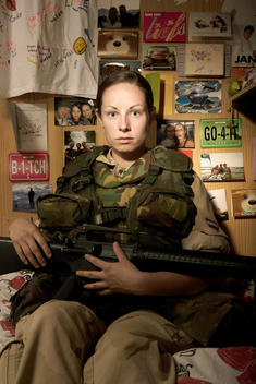 Girl Soldier Sitting On Her Bed Bunk Postcards From Home Hanging On The Wall, Reminders From Home, Holding Her Wweapon M-16 Rifle.