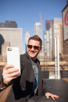 Portrait of business and tech entrepreneur Casey Kerr taking a selfie with his cell phone on the rooftop popular hotel Pod 51 with view of midtown east Manhattan. NYC