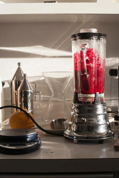 a blender filled with red fruit and vegetables on a kitchen counter