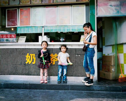 Two young Chinese girls about five years old with their older sister in her late teens in front of a bubble tea shop in a Chinese city.