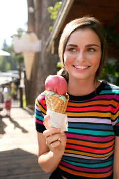 20-something woman in colorful striped shirt holding ice cream cone.
