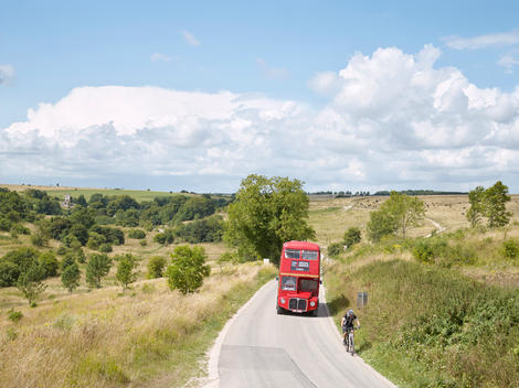 A red bus carries passengers from Imber Village back to a nearby town through Salisbury Plain. Imber is an uninhabited village in part of the British Army\'s training grounds in an isolated area of the Plain. The village remains under the control of the Mi