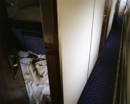 A view down the corridor and inside a room with a woman resting on a bunk bed onboard the Caledonian Sleeper train to Scotland