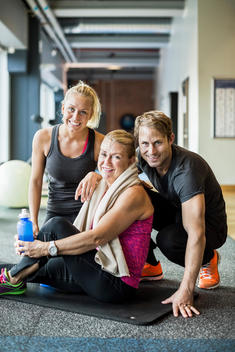Portrait of happy instructors with senior woman at health club