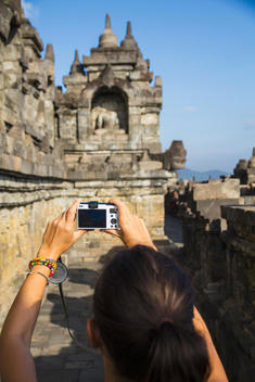 Indonesia, Young woman taking photo of Buddha statue at Borobudur Temple