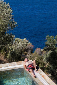 60 year old man relaxing by a pool next to the Mediterranean sea, Kalkan, Antalya, Turkey.