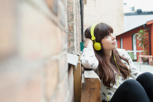 Young woman looking away while listening music at cafe backyard