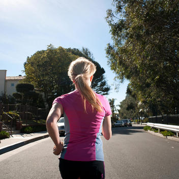 Rear-View Of Woman Running Down Street In Suburbs