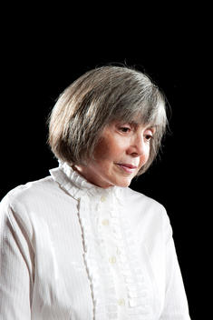 Anne Rice is wearing a white button up shirt as she looks down thoughtfully