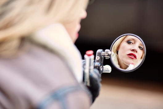 Member of the MissFires all female motorcycle club putting on lipstick in side view mirror