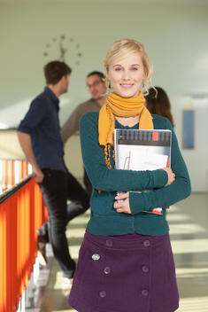 Germany, Leipzig, Young woman holding book with students standing in background