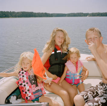 A group of kids and teenagers, who are family (brothers, sisters, and cousins), wearing life vests ride a boat while they take turns skiing and tubing in Lake Tyler, where their family's lake house is located. Tyler, Texas