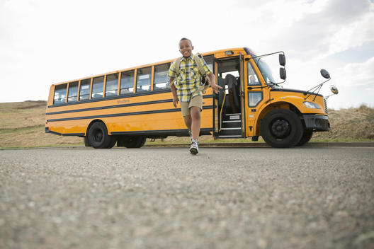 Happy little boy running on road against school bus