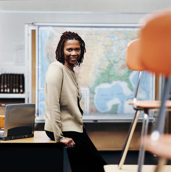 African American teacher sitting on desk in classroom