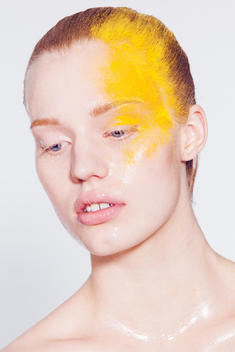 beauty image of model in studio, with vaseline clean skin, hair back and yellow colored makeup dusted on side of the face