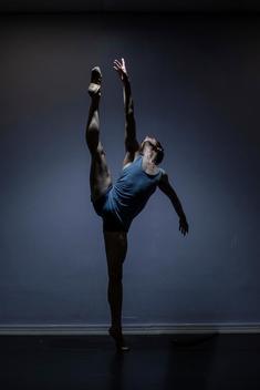 A dancer against a blue backdrop doing a high kick.