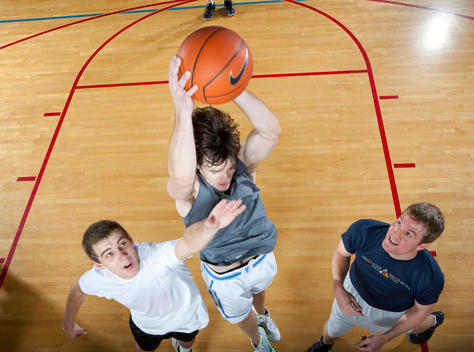 A basketball player jumps to make a shot while others watch or try to block