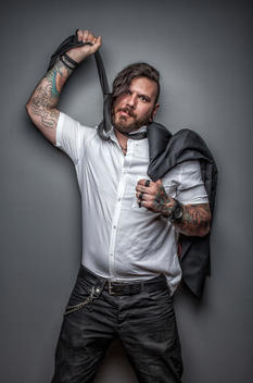 Hipster man with beard and tattoos, pulling his tie like he is choking himself