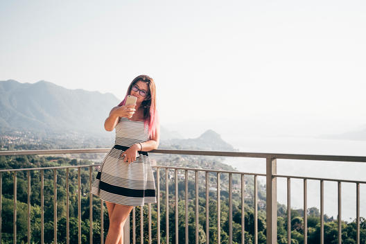 14 year old brunette girl with pink highlights taking selfie with smartphone in front of Lake Maggiore in northern Italy.