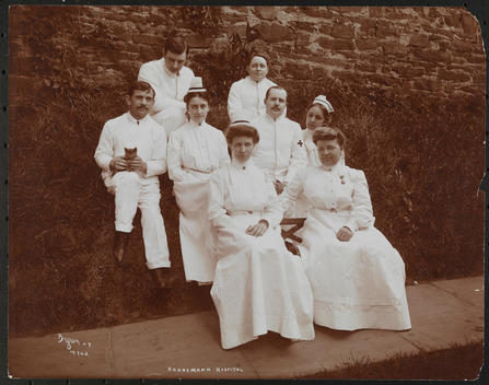 Group Portrait Of Medical Staff Of Hahnemann Hospital, Seated Outside In White Uniforms With One Man Holding A Kitten.