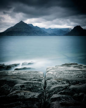 Isle of Skye with calm sea and rocks in foreground under grey sky with long exposure