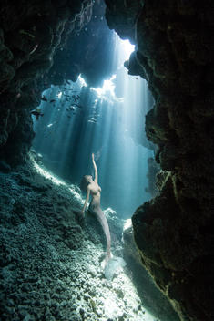 Underwater view of mermaid looking up from sea cave