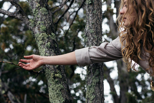 Girl reaching for a branch in the woods.