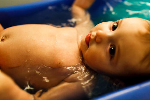 An infant girl relaxes in her bath.