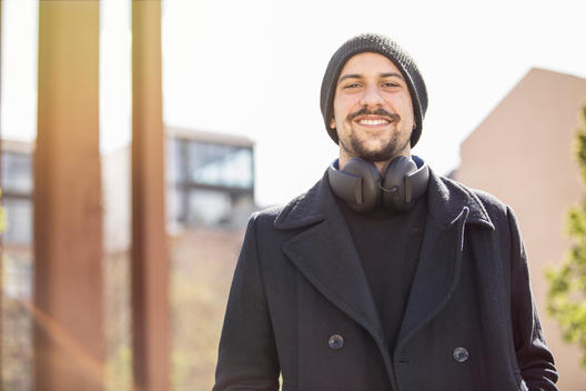 Portrait of smiling young man with headphones wearing wool cap and black pullover