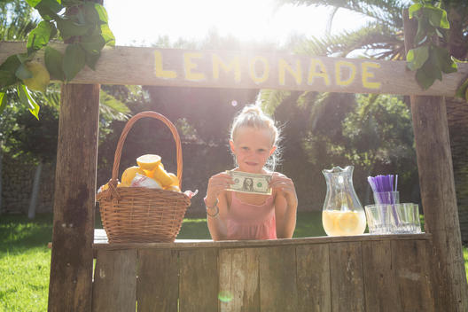Portrait of girl on lemonade stand holding up one dollar bill
