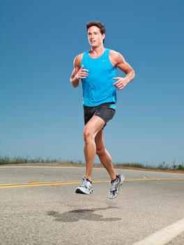 An athletic man is caught mid-air as he is running down the road