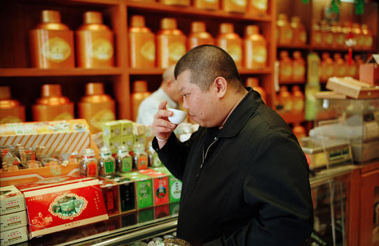 A Man Smells A Small Cup Of Tea In A Chinese Herb Shop.