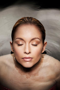 Caucasian woman in her 20\'s with eyes closed submerged to her neck in water