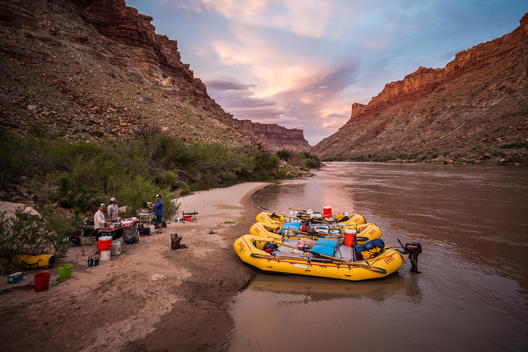 Camp and rafts along a river at sunset.