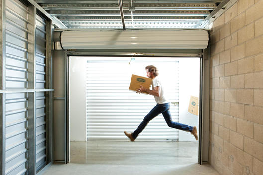Inside a storage facility a man runs past an open unit carrying a box
