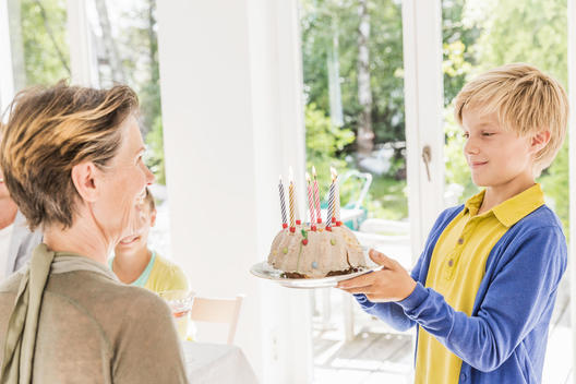 Boy handing birthday cake to grandmother in dining room