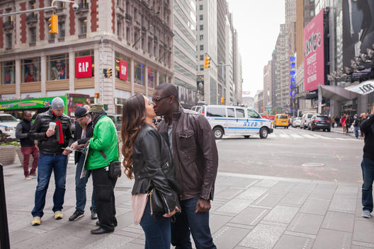 An interracial couple hug and kiss with a police van and crowd of tourists behind in Times Square. New York, NY