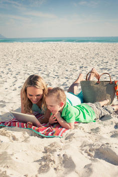 Mid adult mother looking at digital tablet with young son on beach, Cape Town, Western Cape, South Africa