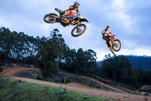 Two dirt bike racers jumping tabletop.