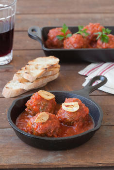 Appeteizer Of Italian Meatballs In Sauce In A Cast Iron Skillet And Baking Pan Seved With Sliced Bread And Wine On A Wood Table.