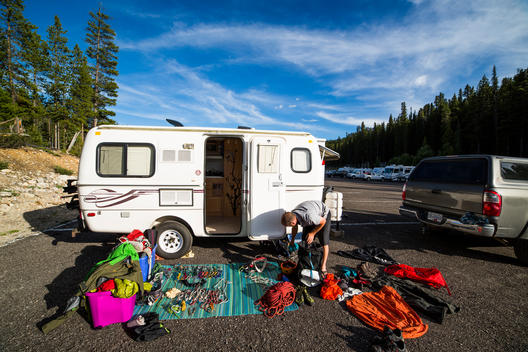 A camper sits in a parking lot in Banff, Canada while a huge pile of climbing gear is laid out in the front.