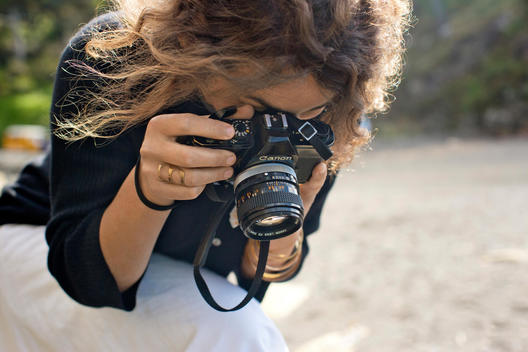 Woman takes photo with vintage Canon camera at beach location.