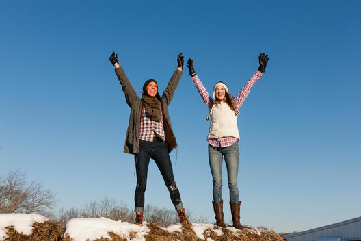 Two young women with arms raised on winter hilltop