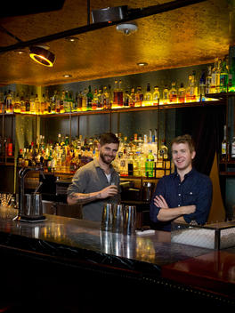Two men stand smiling behind a bar at a pub