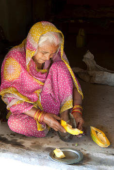 old Indian woman wearing sari sitting on the floor and cutting a papaya