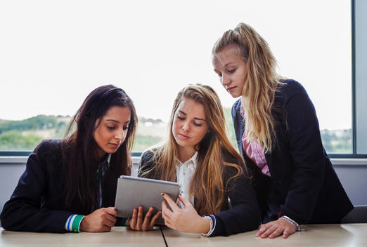 Teenage schoolgirls sitting at desk with digital tablet