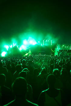 A wide shot of a rave with people in the foreground and an impressive green light show.