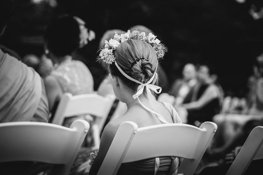 girl with flowers in braided hair sitting on a wooden chair during the wedding ceremony